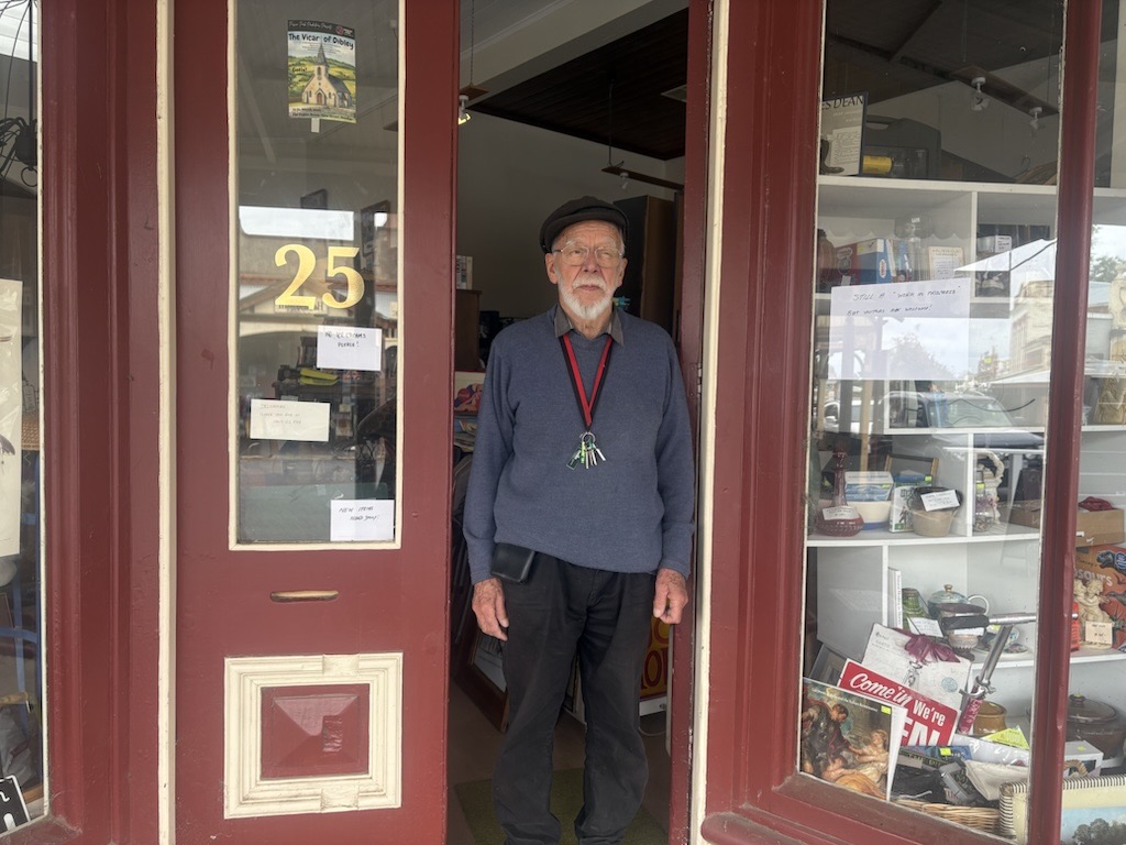A man with a white beard and a flat-cap in the doorway of a bookstore. 