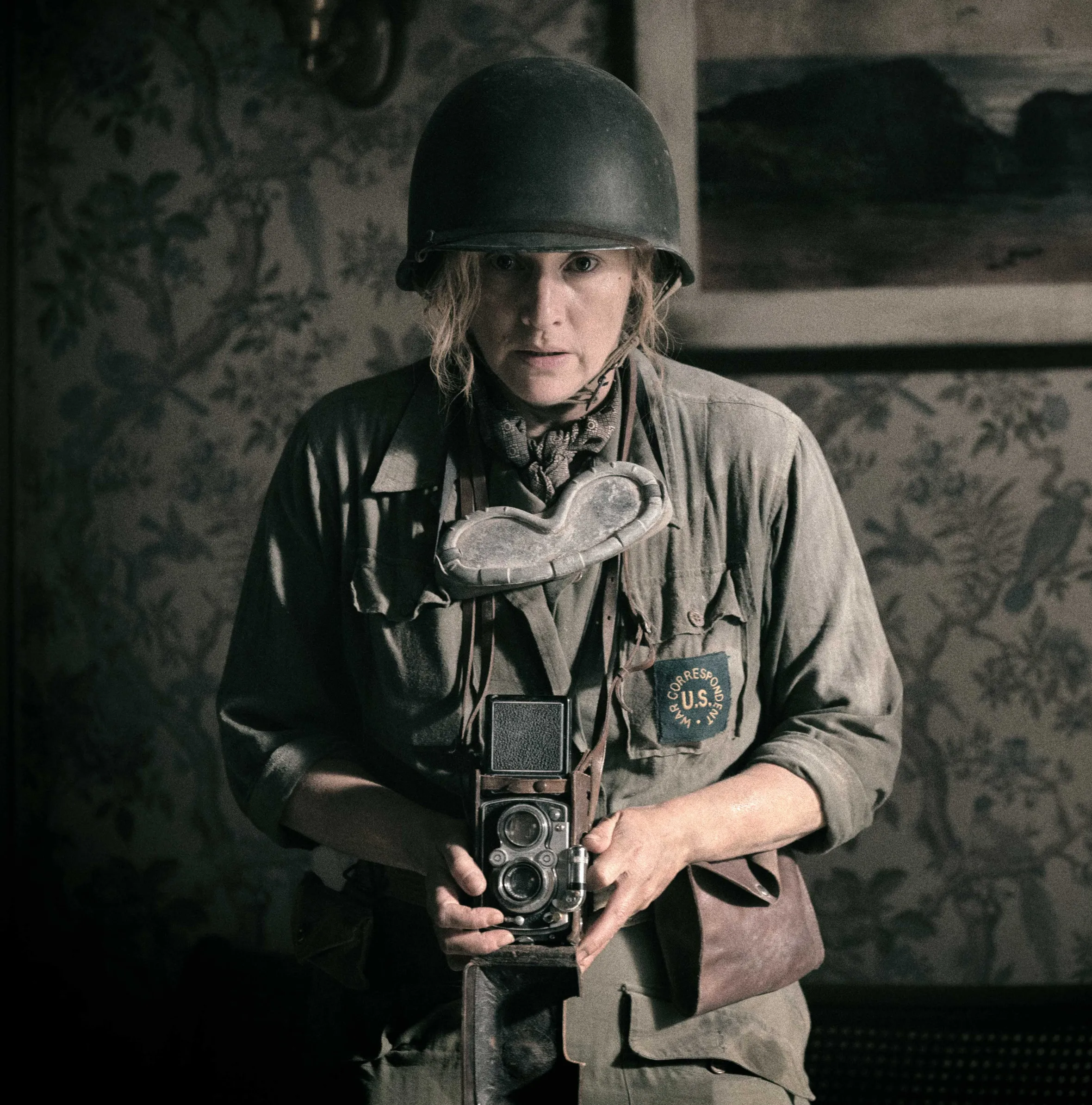 Kate Winslet as Lee Miller, a WWII correspondent, holding a Rolleiflex camera.