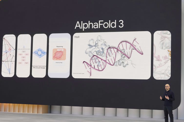 A man standing before a giant presentation screen depicting a DNA double helix and the word AlphaFold 3