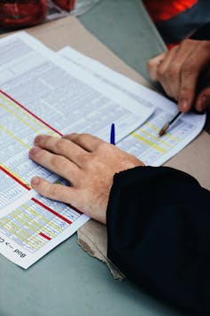 A close-up of a person's hands, with pen in one, going over a complicated medical billing form.