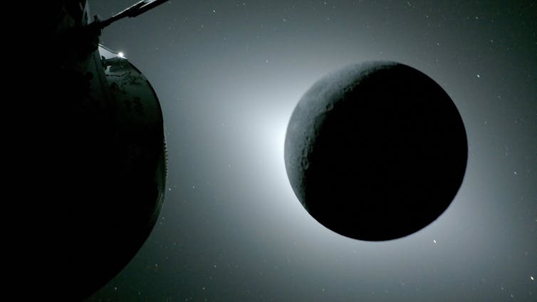 An eclipse visible from space - the Moon is shown shadowed with some sunlight visible behind it, and part of the Orion capsule shown off to the left.