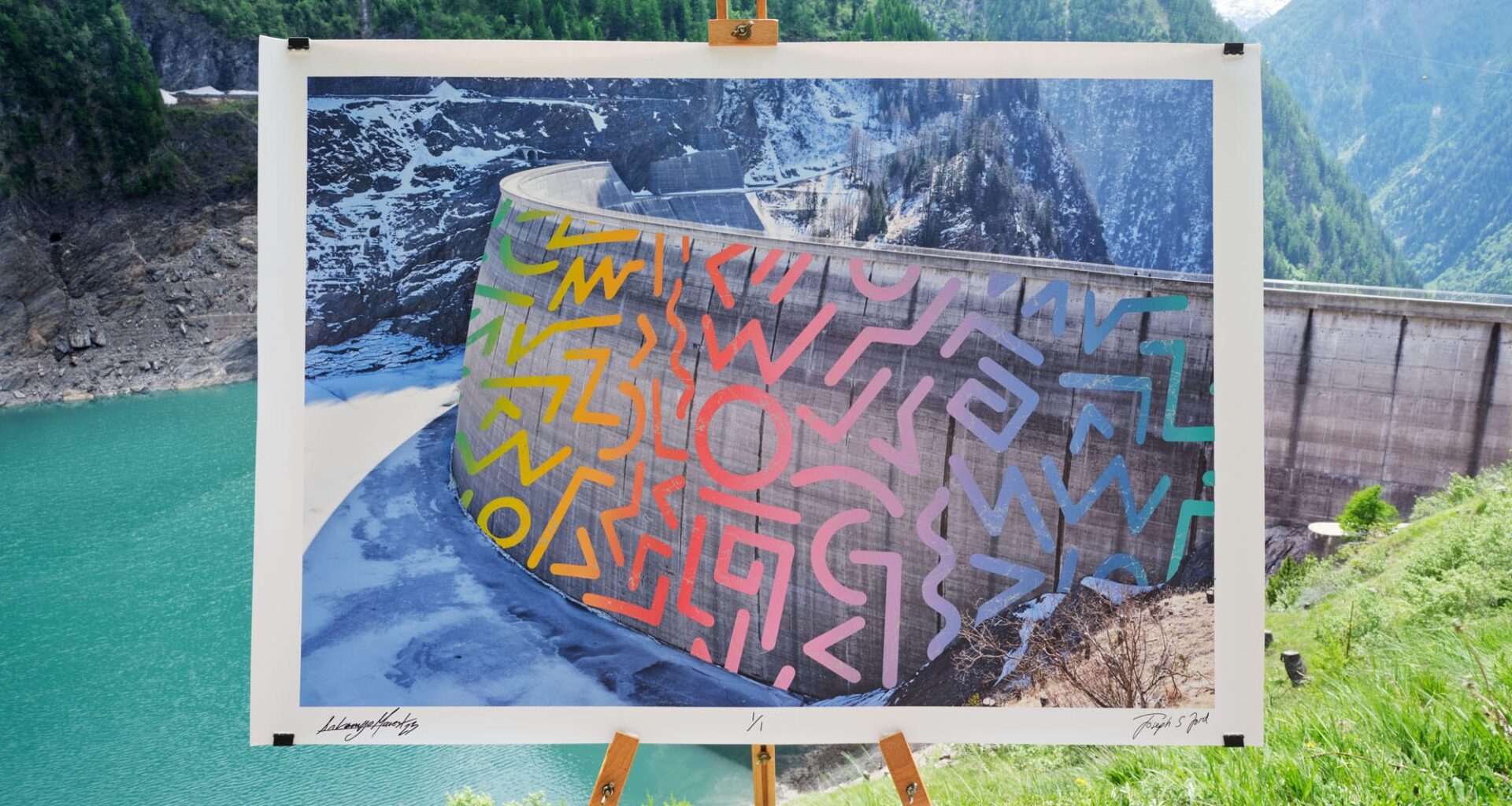 A photographic print of a dam in Switzerland with a street art intervention superimposed on the image, which is photographed on an easel in front of the same landscape