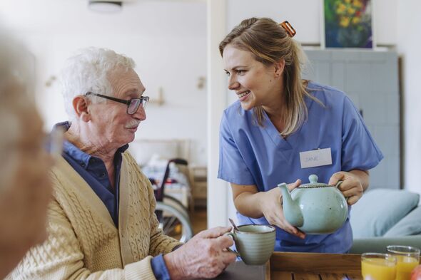 Happy healthcare worker holding teapot and talking to senior man at table Happy healthcare worker holding teapot and talking to senior man at table