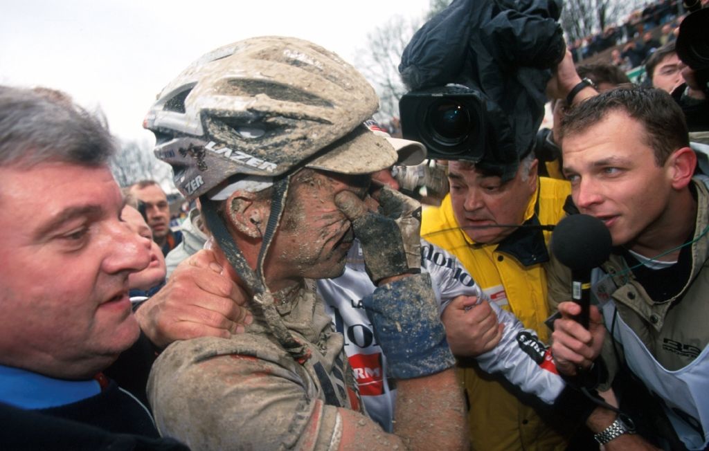 Servais Knaven, covered in mud and surrounded by cameras and reporters, holds his face in disbelief after winning Paris-Roubaix 2001