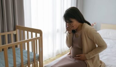 Pregnant person on bed next to crib holding mouth and stomach