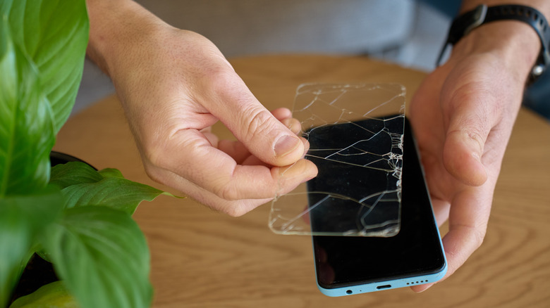 A man hlding a carcked screen protector above a smartphone