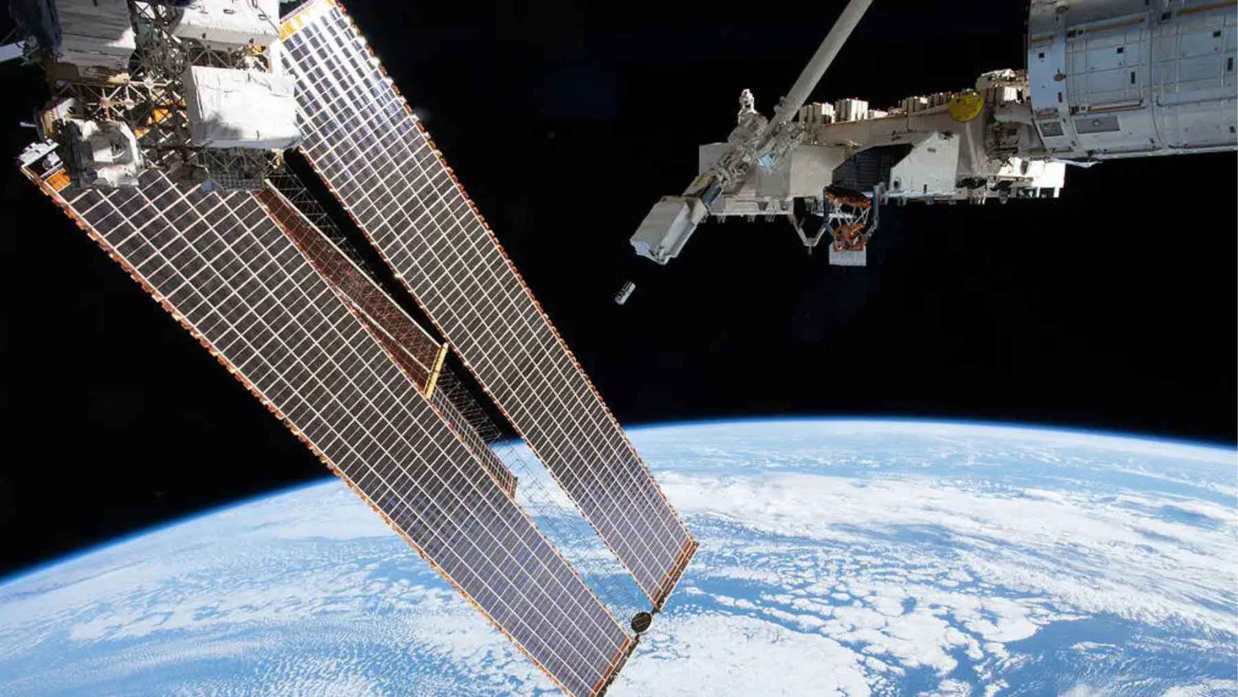 International Space Station solar panels extending over Earth with clouds and horizon visible from low Earth orbit