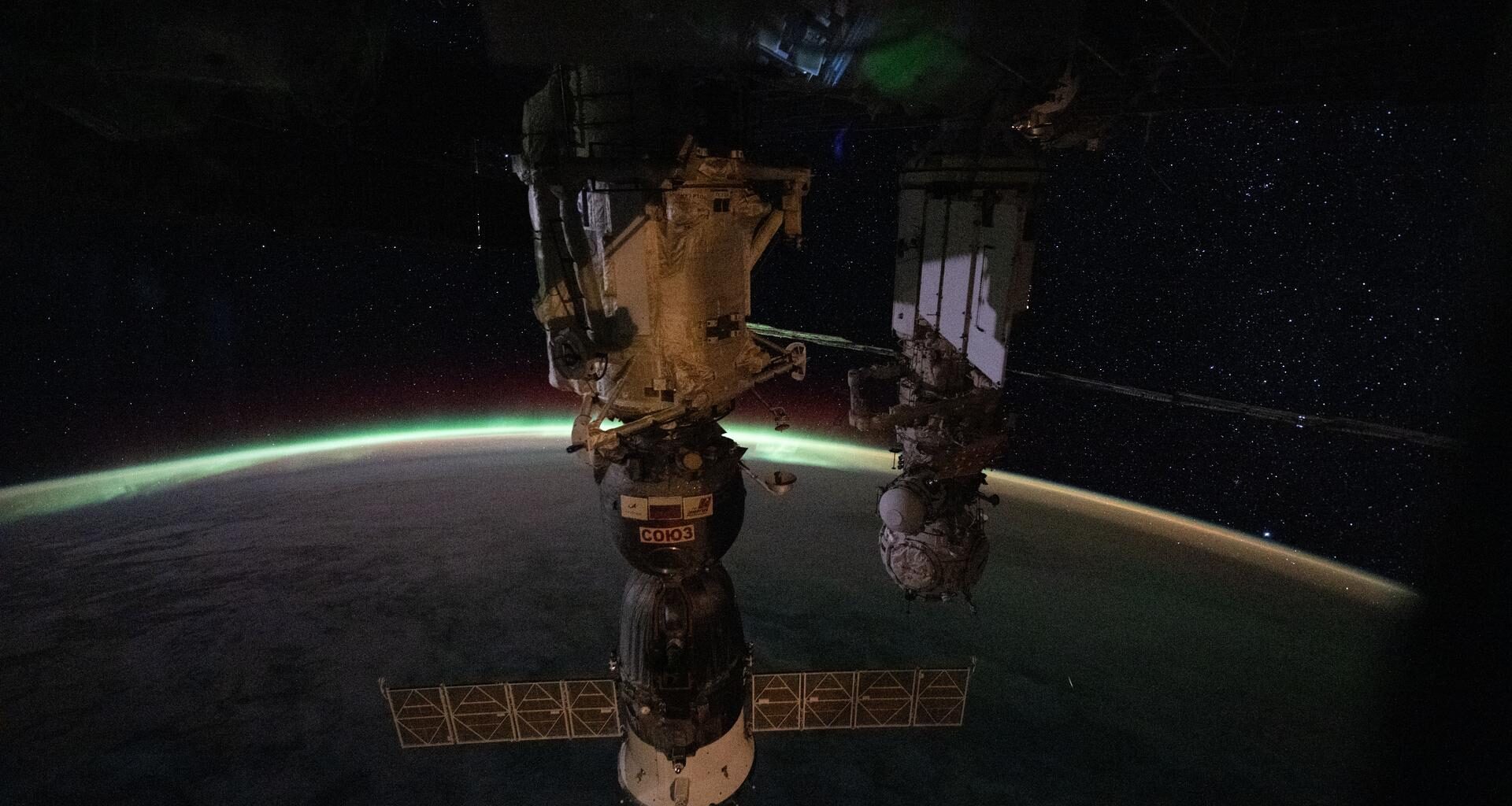 The aurora australis arcs above Earth’s horizon and fades into the airglow as the International Space Station orbited 265 miles above the Indian Ocean east of Perth, Australia, at approximately 2:03 a.m. local time. In the foreground, the Soyuz MS-28 crew spacecraft is shown docked to the Rassvet module. In the background, the Pirs docking module is attached to the Nauka science module.