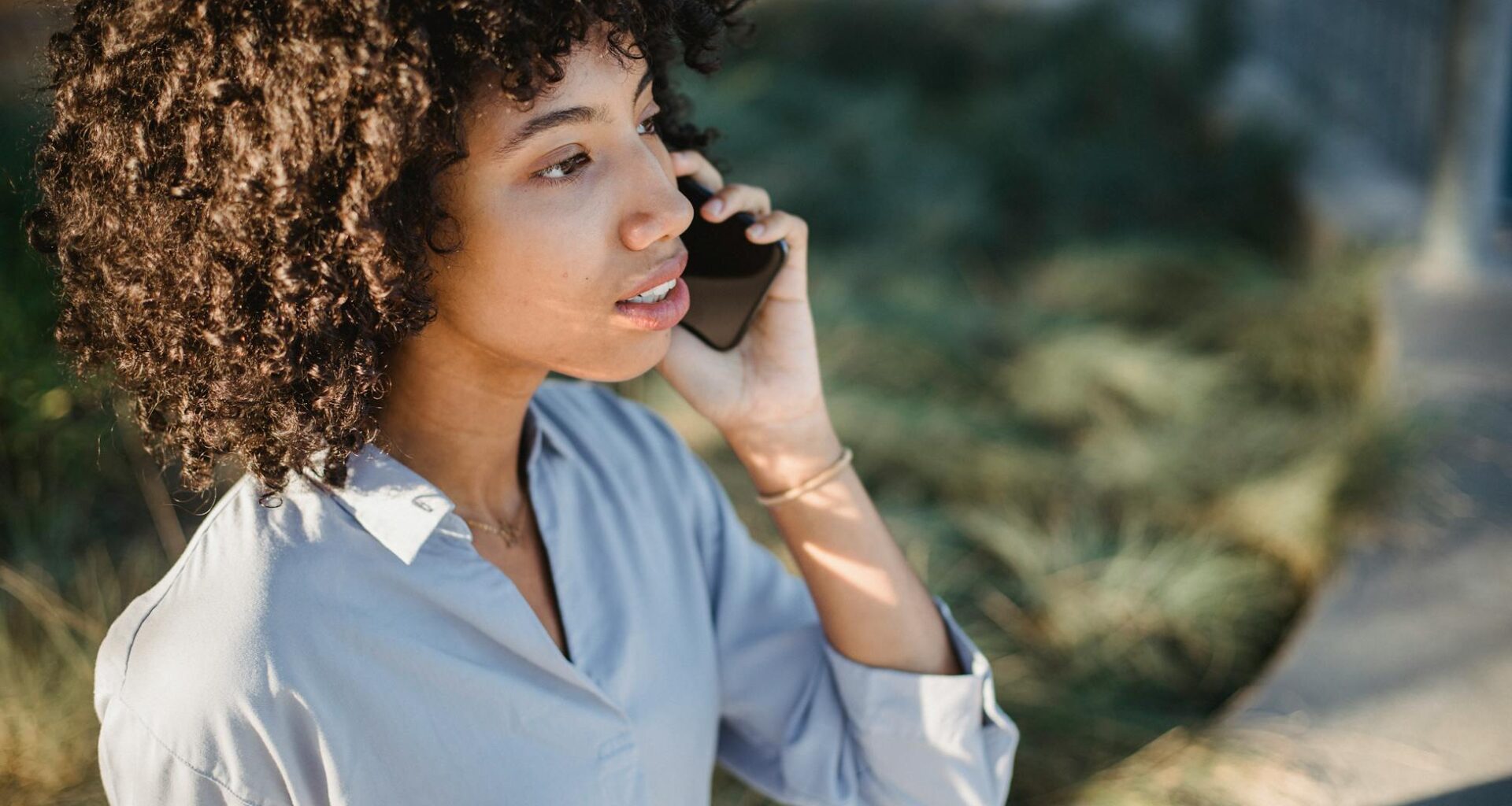 Crop African American female in casual clothes standing on street and talking on smartphone while looking away
