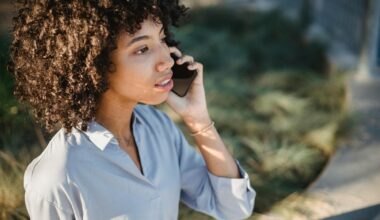 Crop African American female in casual clothes standing on street and talking on smartphone while looking away