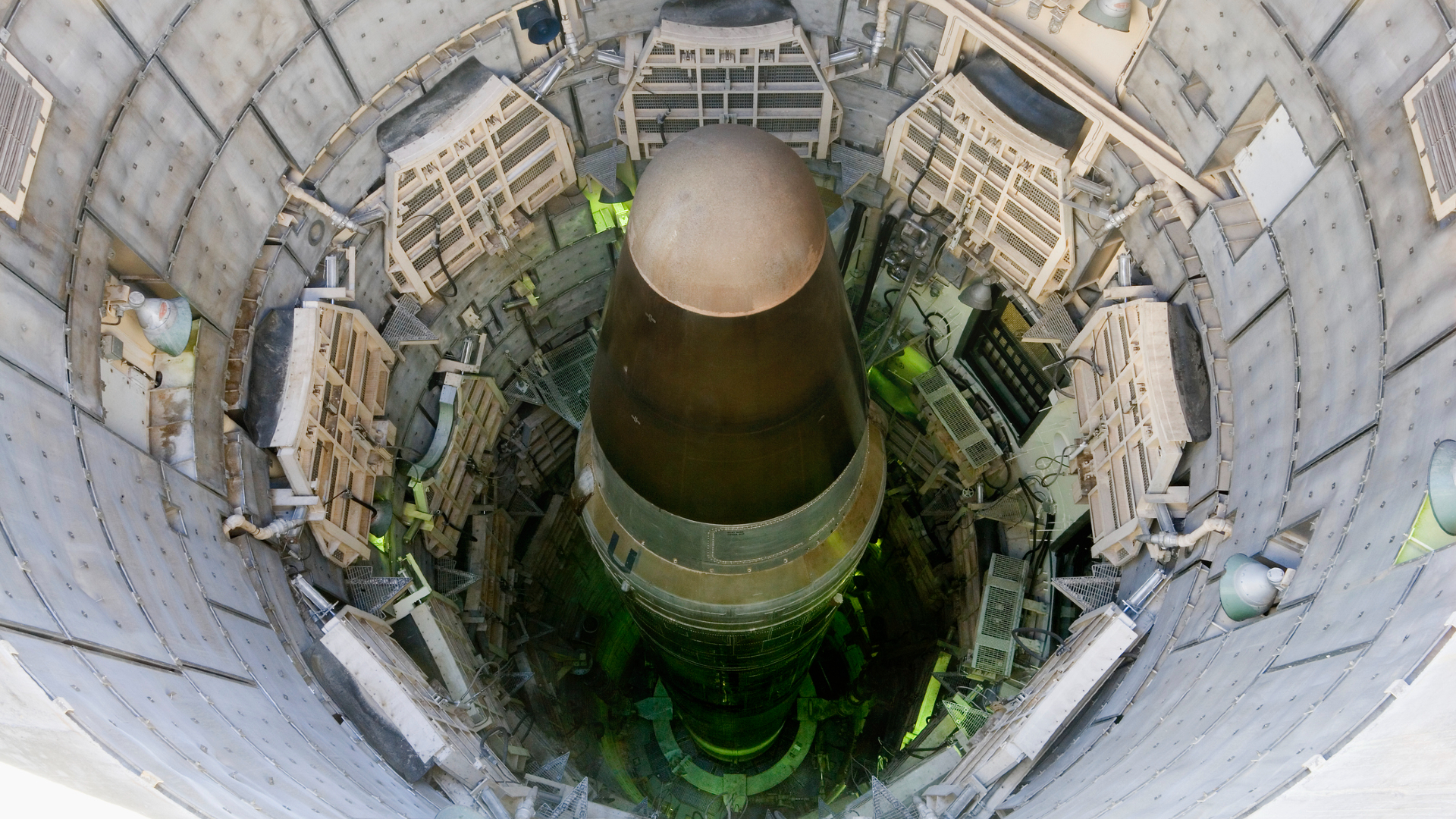 A large metal missile is seen down in a tall cylindrical missile silo.