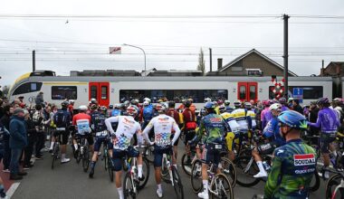 Riders wait at a level crossing for a train to pass during the 2026 Tour of Flanders