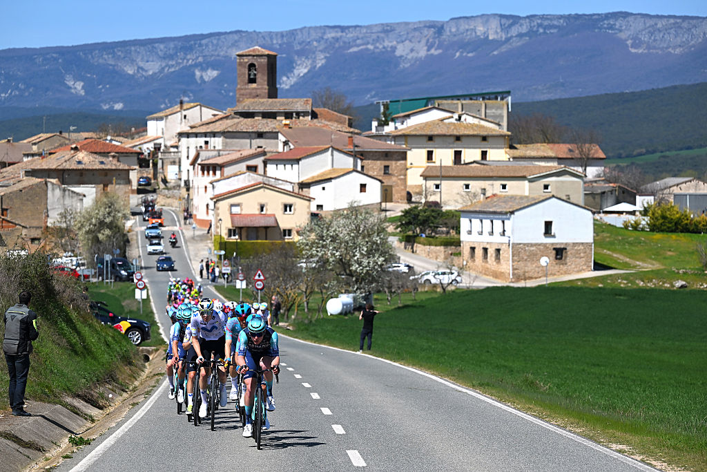 The peloton riding up a two-lane road heading out of a town