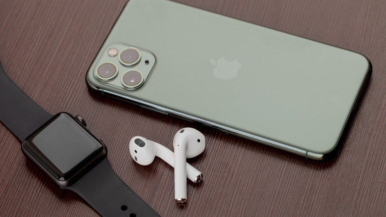 An Apple Watch and a pair of AirPods sitting next to an Apple iPhone on a wood surface
