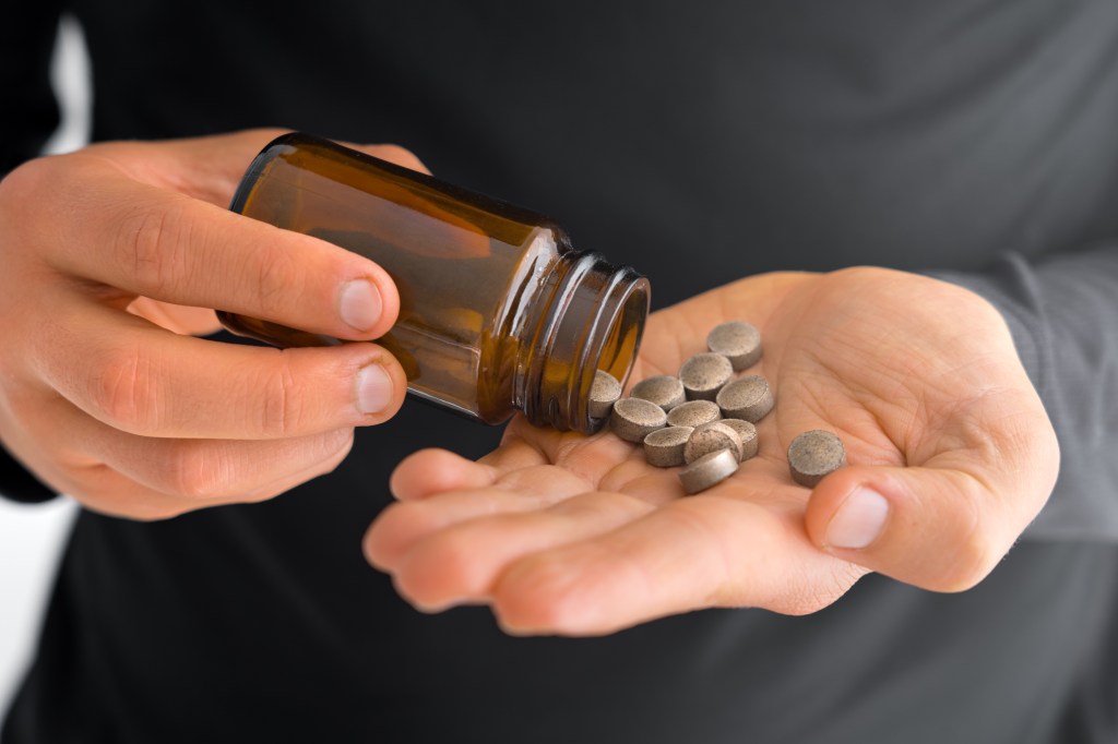 Hands pouring iron supplement pills from a bottle.