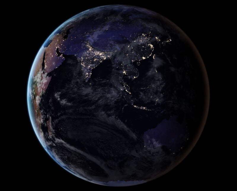 A view of Earth from space at night, showing city lights across Asia, Australia, and parts of Africa, with dark oceans and clouds visible under a black sky.