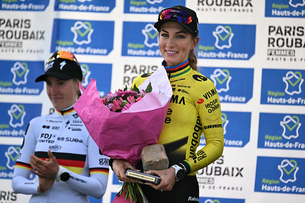 Pauline Ferrand-Pr&eacute;vot smiles on the Paris-Roubaix podium, holding a bouquet of flowers and a cobble trophy