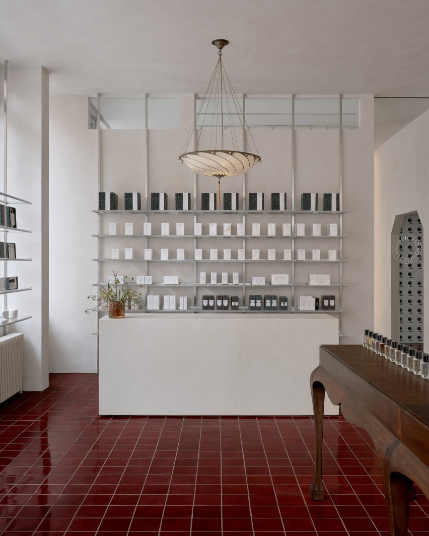 Lime-washed walls and minimalist metal shelving contrasts oxblood tiles inside a perfume store