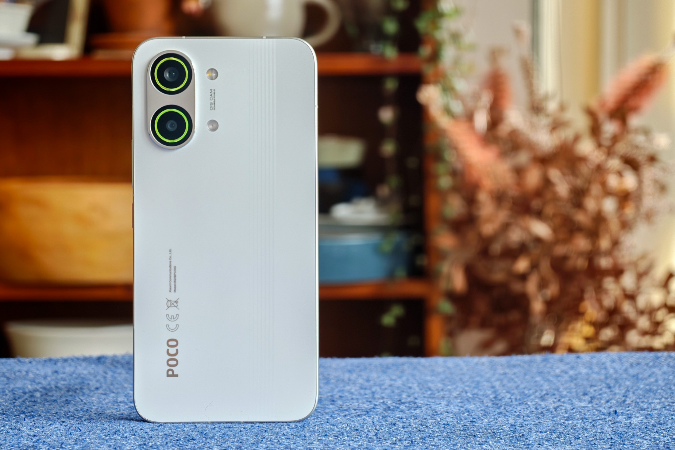 Photo of Poco X8 Pro Max standing on a blue tablecloth with the RGB lights on