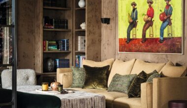 a burl wood clad sitting area with built in shelving, a beige couch and a painting of cowboys on the wall