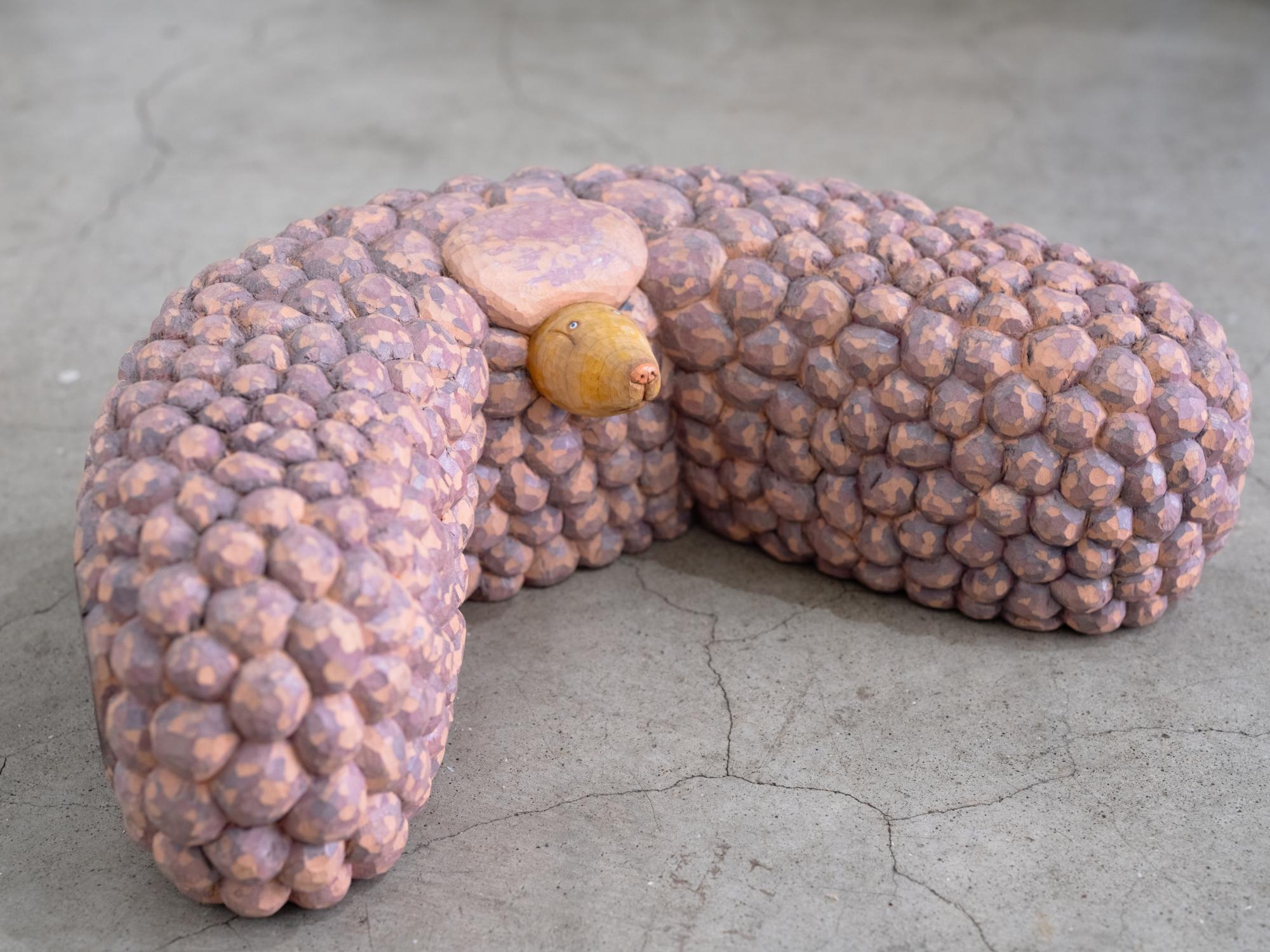 a pink wood-carved sculpture of a dog by Misato Sano