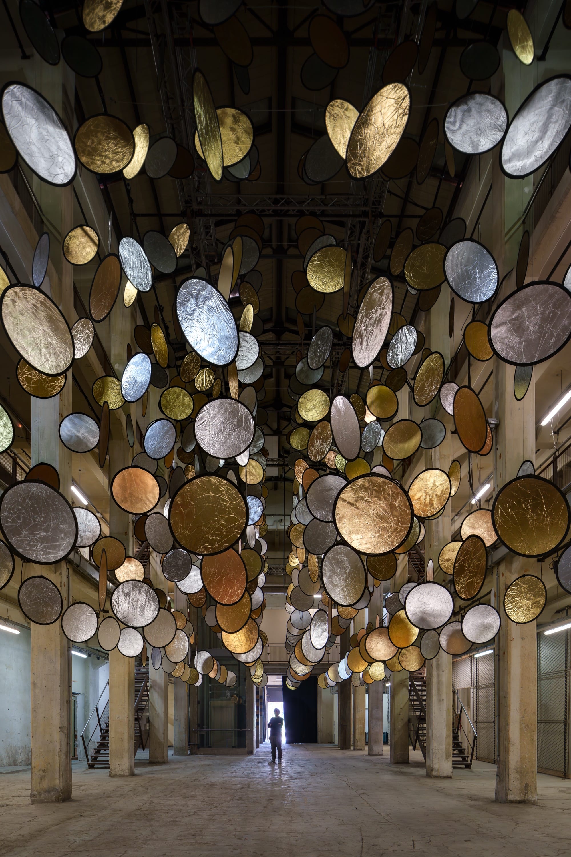 A large interior installation of metallic discs hanging from the ceiling in an industrial space