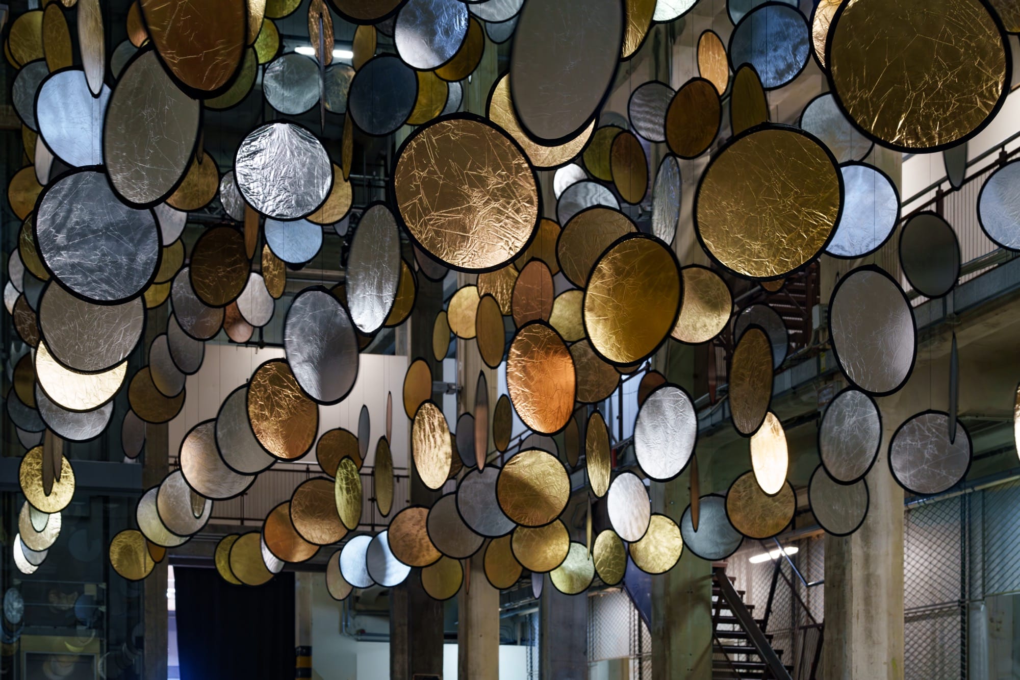 A large interior installation of metallic discs hanging from the ceiling in an industrial space