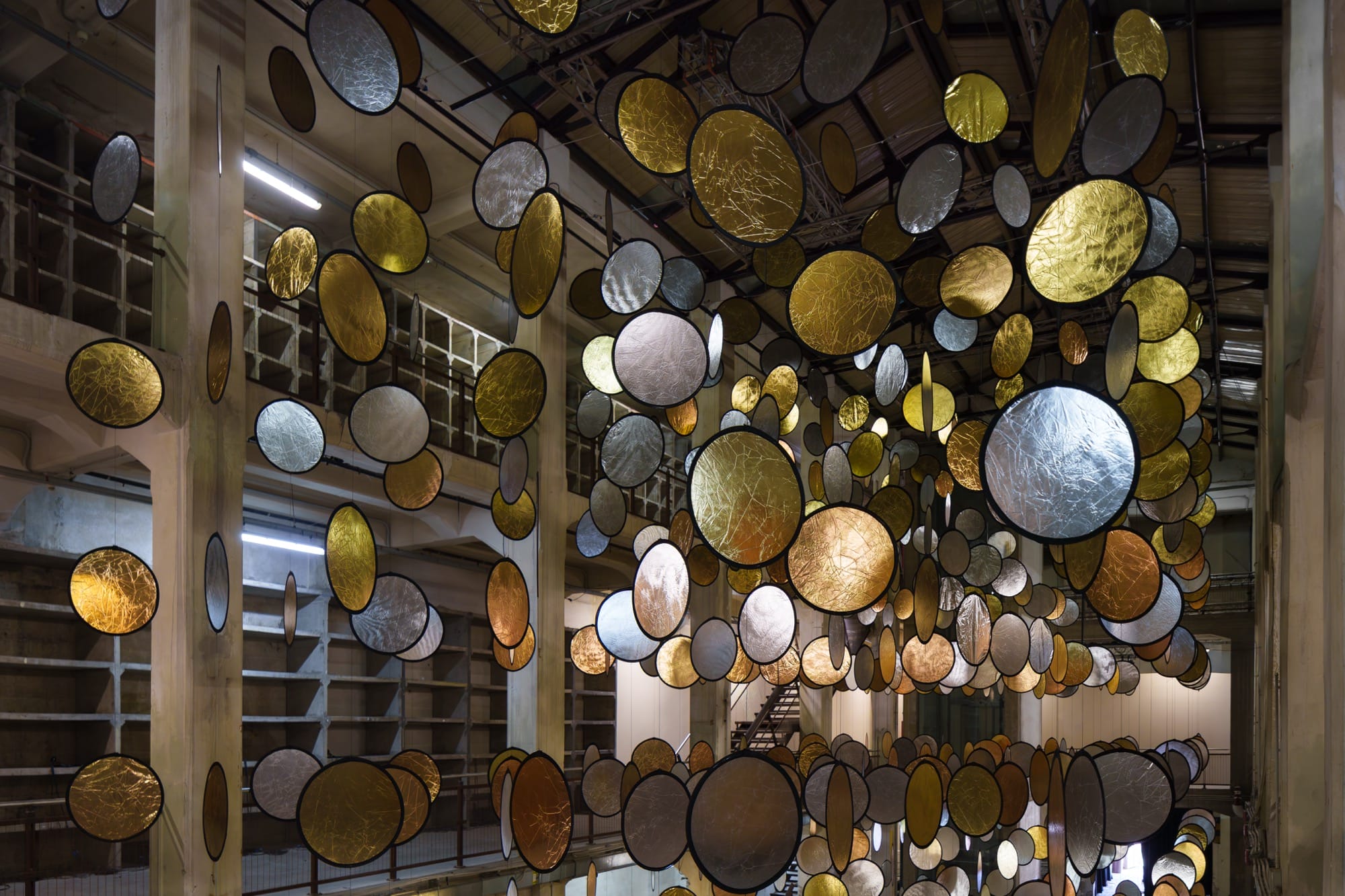 A large interior installation of metallic discs hanging from the ceiling in an industrial space