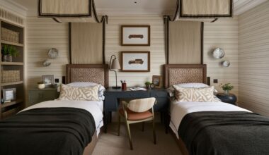 a twin children's bedroom with beige striped walls and two canopy twin beds, a desk in the middle, a bookcase, and dark green blue color pops
