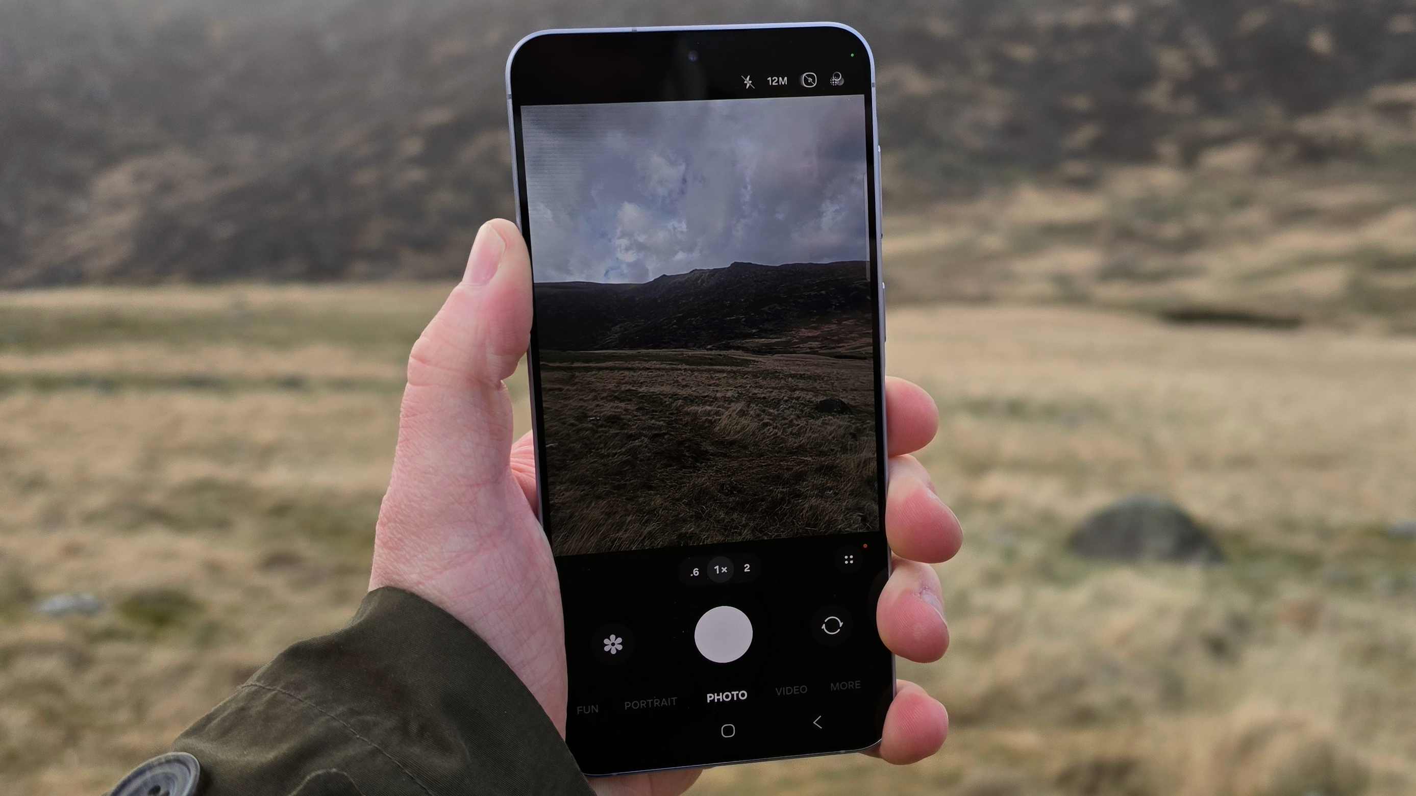 The Samsung Galaxy A57 being held over a field, showing its camera viewfinder.