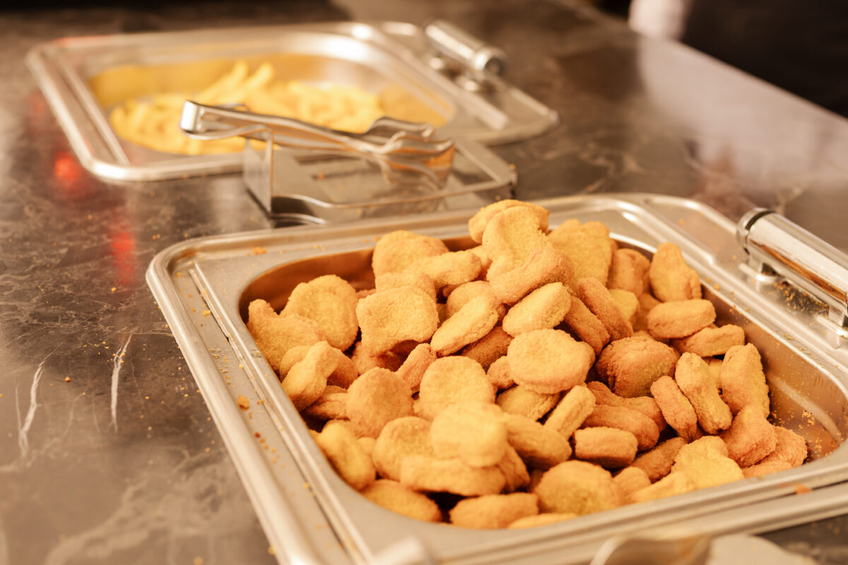 Photo shows a large silver serving tray full of chicken nuggets next to a matching container of french fries. The UK government is expected to announce a ban on fried foods such as chicken nuggets, battered fish and chips, and jam doughnuts in school dinners