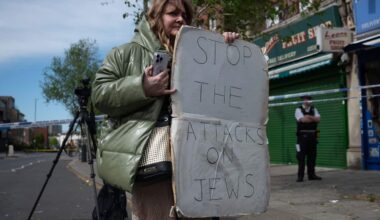 A woman holding a protest sign that says "STOP THE ATTACKS ON JEWS".