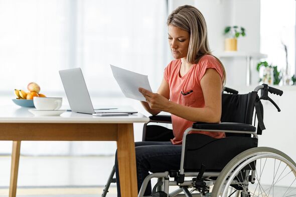 Woman in a wheelchair working on paperwork and laptop at home.