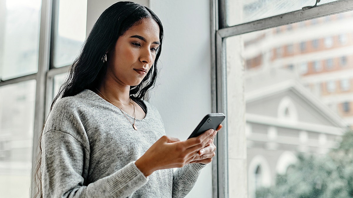 Woman using a mobile phone by a window indoors