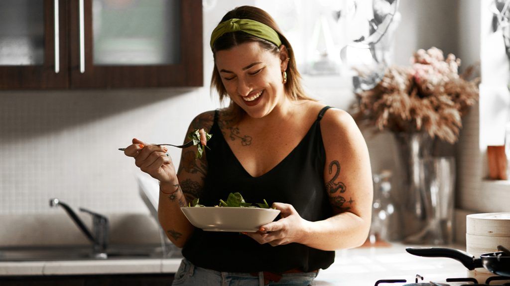 smiling white woman with arm tattoos eating fresh food from a bowl