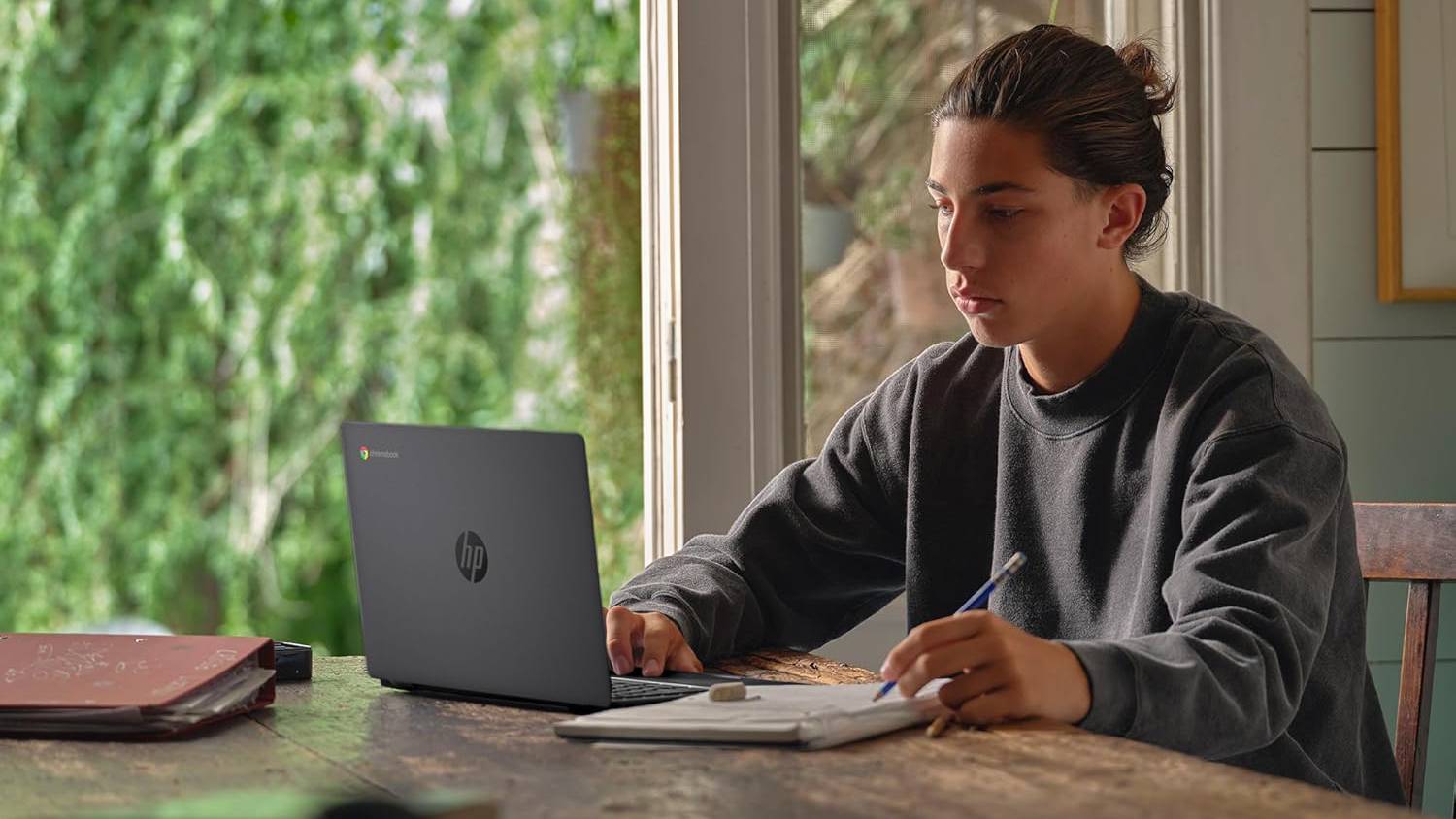 Person using HP Chromebook 14 on kitchen table while writing on notepad