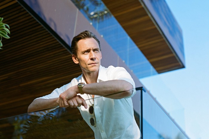 The Night Manager Tom Hiddleston in The Night Manager. He is outside a building leaning on a glass wall. He wears a white shirt