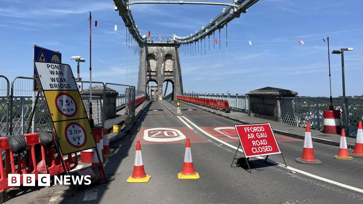 The bridge closed off by orange traffic cones and road closure signs on a sunny day.