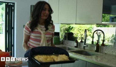Joanna  holds a baking tray containing fresh challah bread in a kitchen.