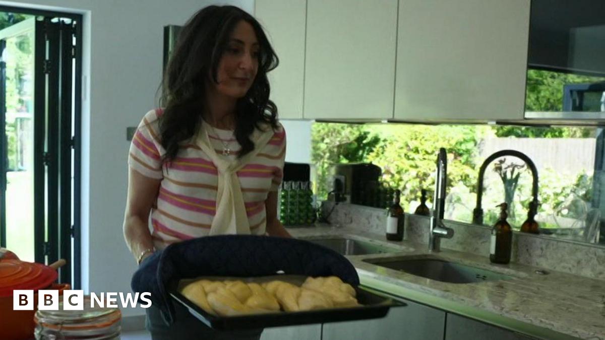 Joanna  holds a baking tray containing fresh challah bread in a kitchen.