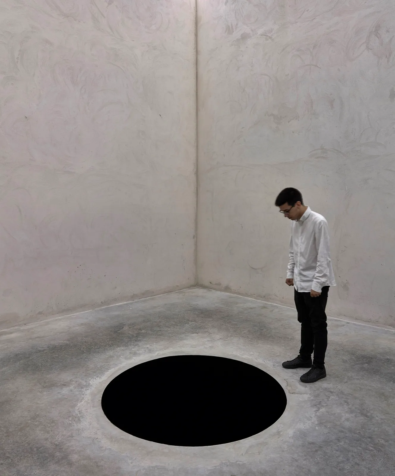 A man looks down at a black hole in the floor as part of Anish Kapoor's "Descent into Limbo" exhibit.