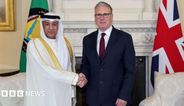 Keir Starmer and Jasem Mohamed Albudaiwi shaking hands in front of a marble fireplace in Downing Street. The UK and GCC flags are behind them.