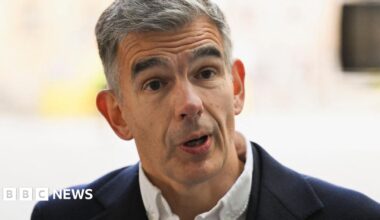 Matt Brittin looks at the audience while standing and speaking onstage against a blue background  in London in 2016.