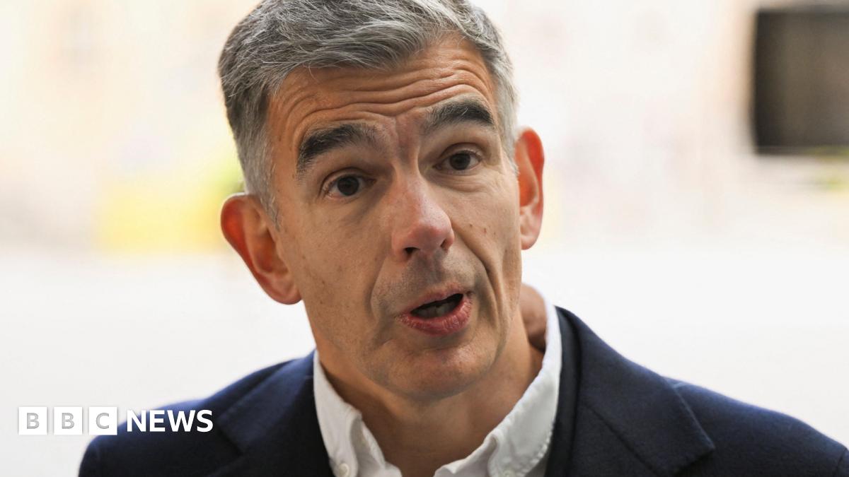 Matt Brittin looks at the audience while standing and speaking onstage against a blue background  in London in 2016.
