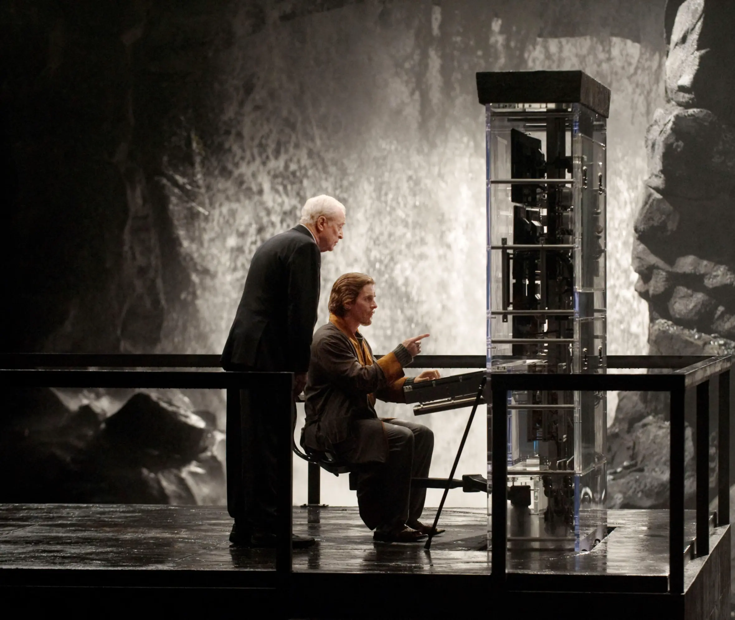 Michael Caine as Alfred and Christian Bale as Bruce Wayne, looking at a device in The Dark Knight Rises.