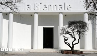 A white building bearing the words "la Biennale" with a black tree in front of it.