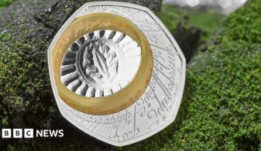 Both sides of the coin shown on a fake background of granite grey rock frosted in green lichen. The back of the coin on the left is silver with an etching in a Lord of the Rings script and language. A gold band, the one ring, is also inscribed in an Tolkien language, and sits slightly to the top left corner of the seven sided coin. it surrounds the eye of sauron, a slit etched onto the silver with an oval around it that is then surrounded by a fan of lines to the ring, making it look like the sun. the face of the coin, the right is the same as a 50p coin with a King Charles the third profile and the visible inscription fromt he top clockwise of G Rex   F D 50 pence 2026 Char with the rest of the king's name obstructed by the back of the coin.