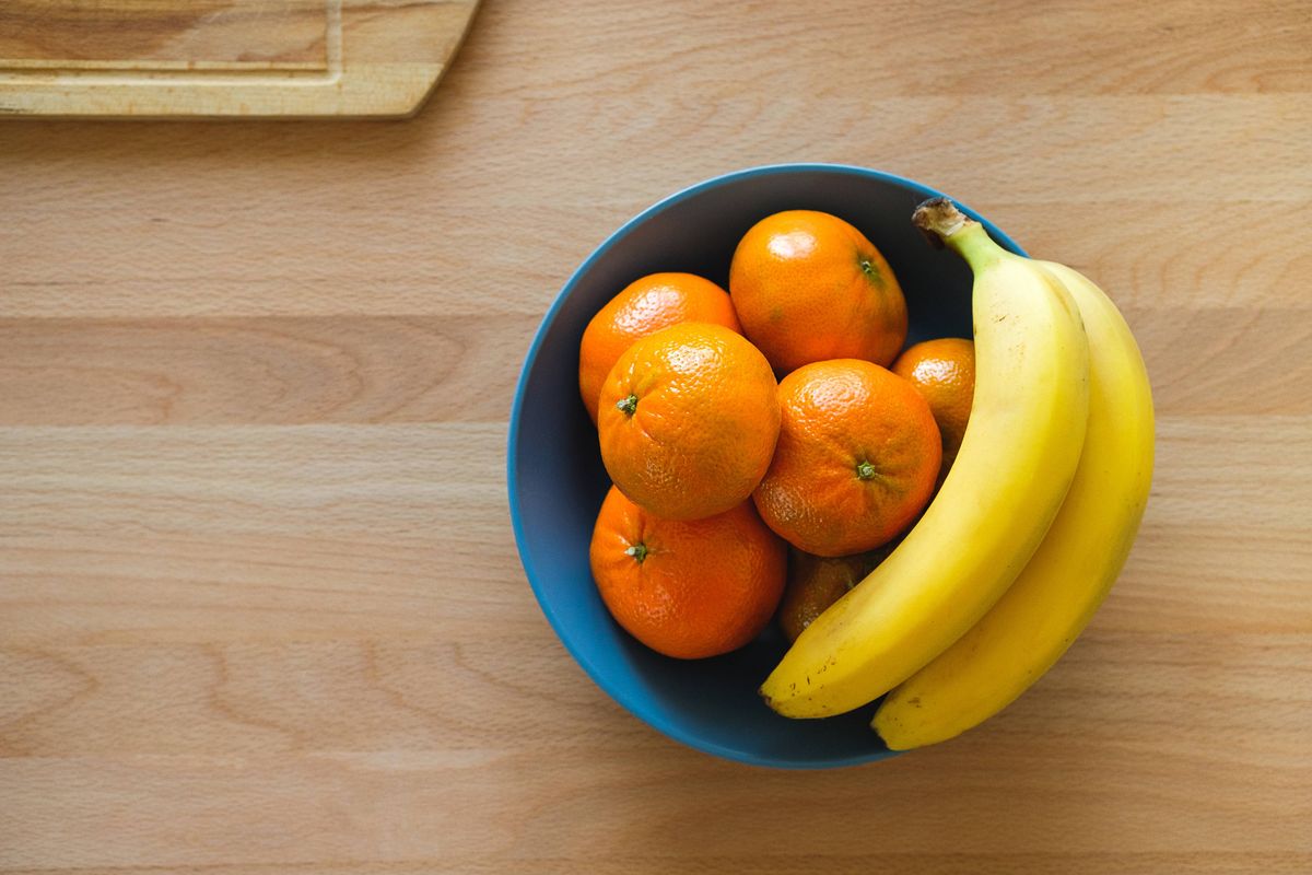 A Bunch Of Yellow Bananas, Bright Orange Tangerines. Healthy Fruits In A Ceramic Plate, Against The Background Of A Wooden Kitchen Table. Vegetarian, Vegan, And Raw Food.