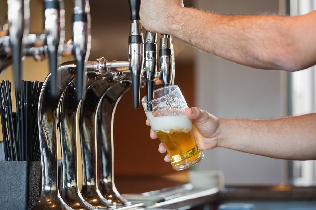 An individual is engaged in the process of pouring a beverage from a tap into a glass, within a bar setting.