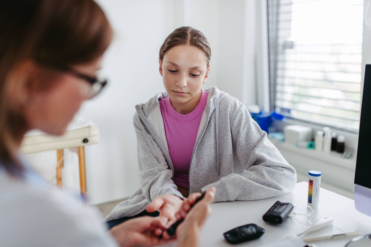 Diabetologist doctor taking finger-prick blood sample for glucose testing in diabetes clinic. Teenager girl diagnosed with diabetes testing her blood sugar.